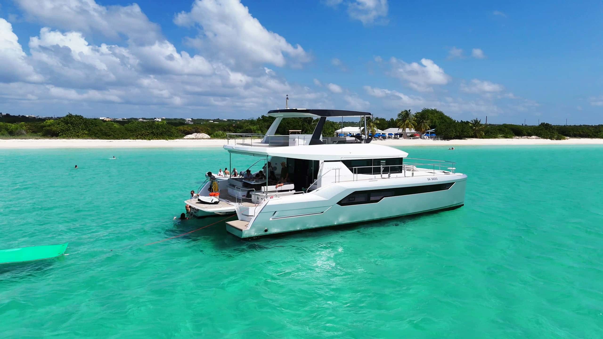 The 53’ power catamaran at anchor off a white-sand beach, guests in the aft cockpit